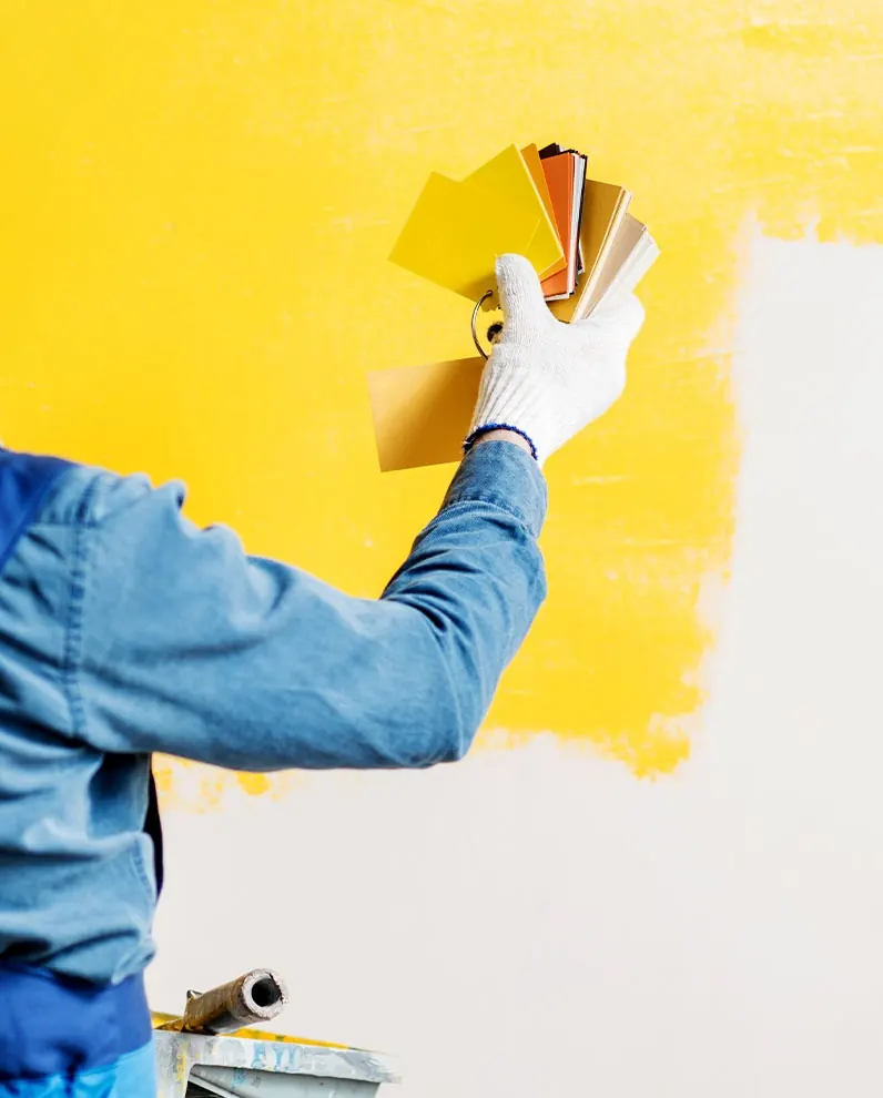 Peintre tenant un nuancier devant un mur peint en jaune